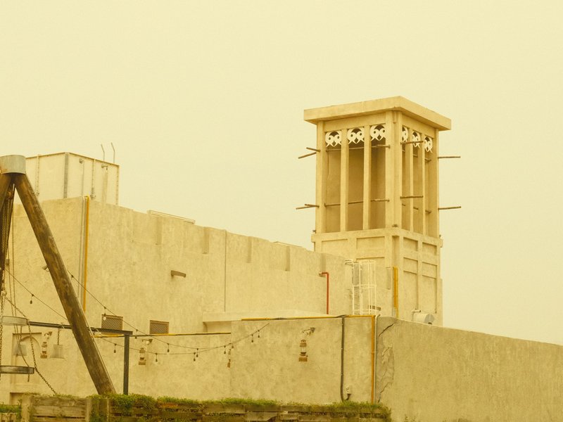 A yellow-tinted image of a traditional wind tower on a building against a hazy sky.