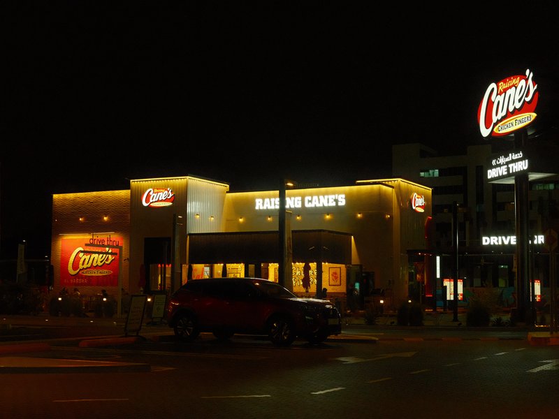 Night view of a fast-food restaurant with illuminated signage and a parking lot.
