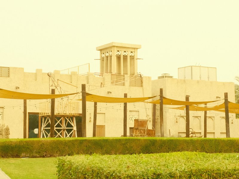 A yellow-tinted image of a building with classical architecture, surrounded by green shrubs and yellow fabric drapes.