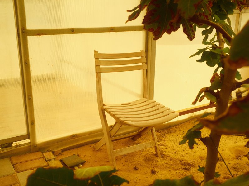 A wooden chair in a sandy indoor setting with yellowish light filtering through glass.