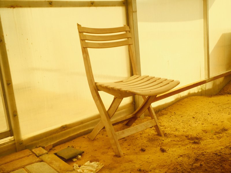 A wooden chair positioned in a sandy indoor space with soft yellow lighting.