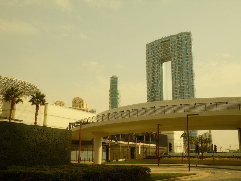 Modern urban architecture featuring tall buildings and a curved overpass under a hazy sky.