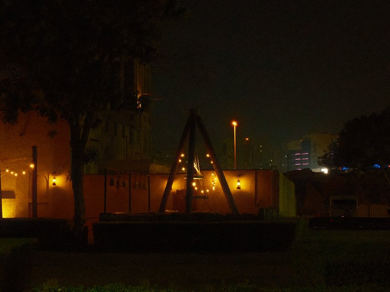A dimly lit playground swing set at night with soft orange lights in the background.