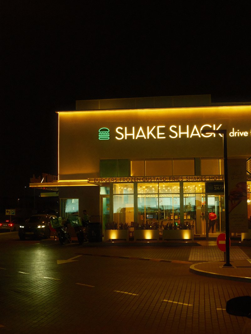 Night view of a Shake Shack restaurant with illuminated signage and a drive-thru.