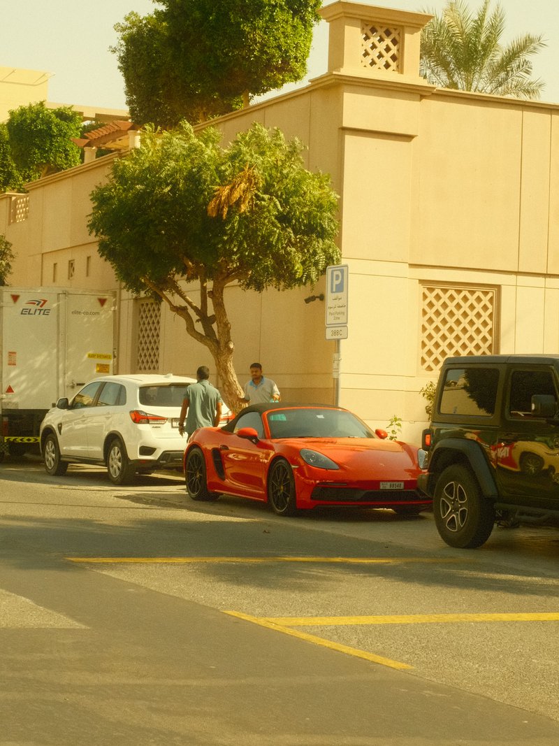 A red sports car parked on a city street with palm trees and buildings in the background.
