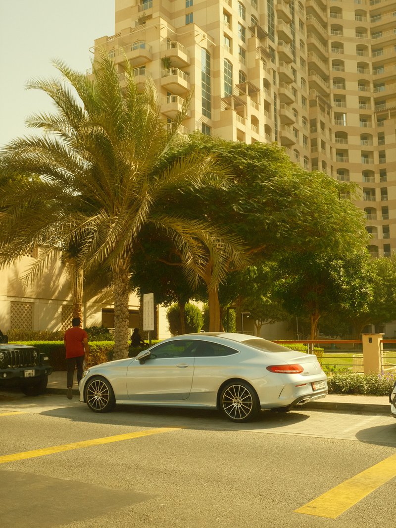 A sleek white car parked on a street lined with palm trees and tall buildings under a sunny sky.