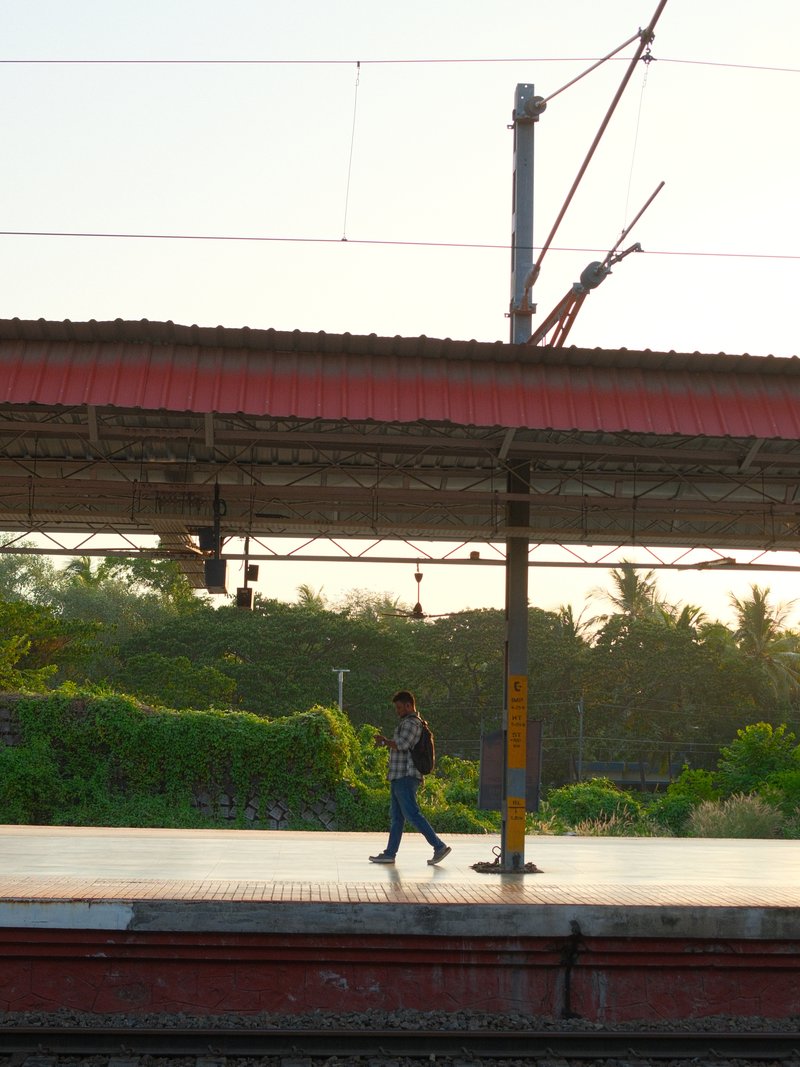 A lone figure walking on a train platform during sunset, surrounded by lush greenery.