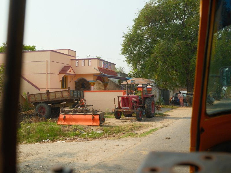 A view of a rural street with parked tractors and a residential building in the background.