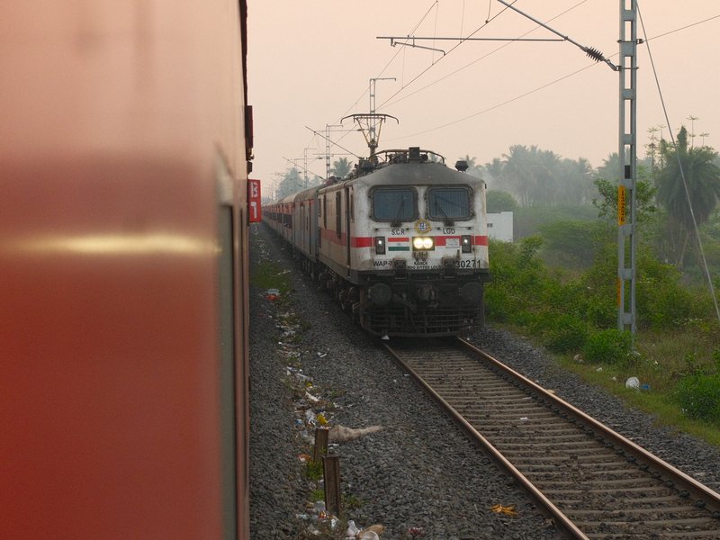 A train approaching on tracks with greenery in the background during a hazy evening.