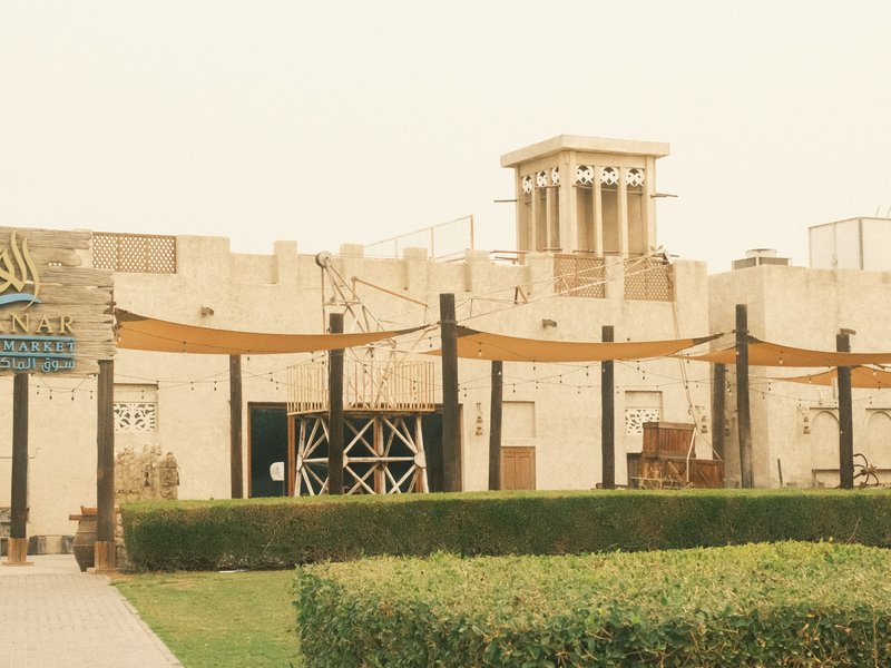 A sandy-colored architectural structure with a tower and wooden awnings in a landscaped area.