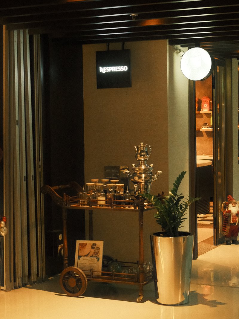 A cozy cafe entrance with a decorative cart and a potted plant, illuminated by soft indoor lighting.