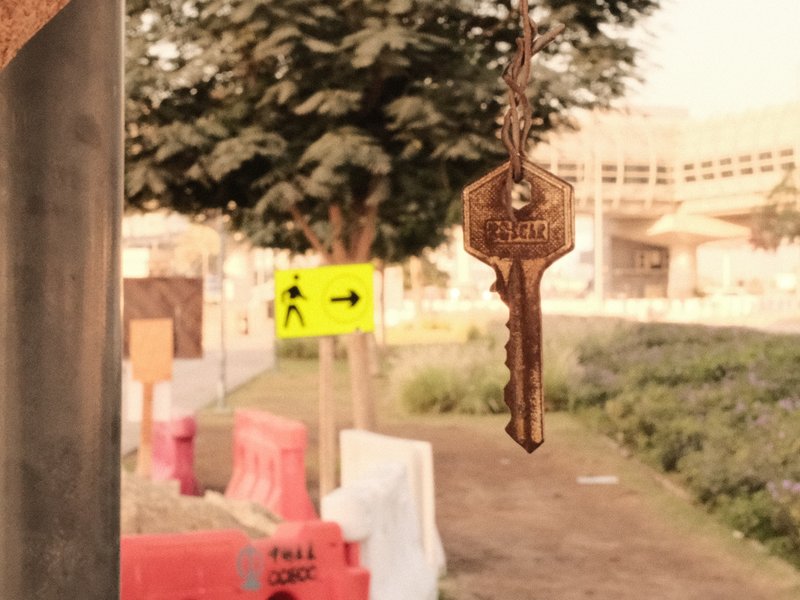 A close-up of a key hanging in focus with a blurred urban construction site in the background.