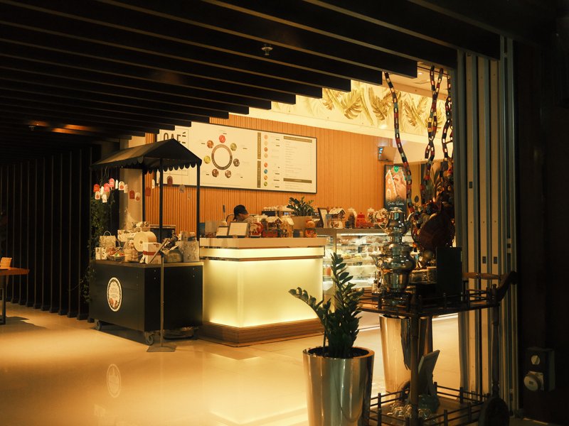 A cozy indoor café with warm lighting and a display of pastries and drinks.