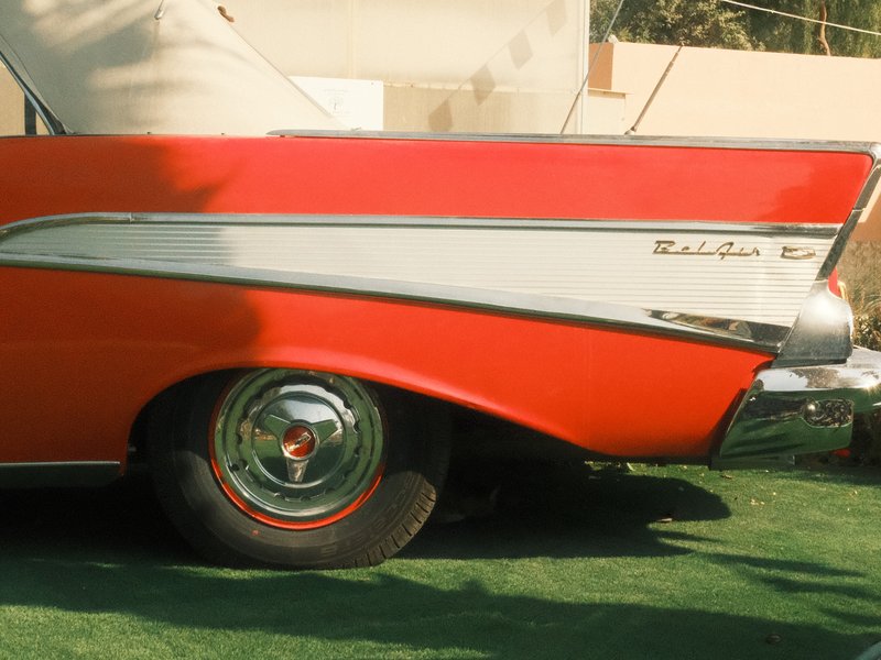 Close-up of a vintage red car's rear fin and wheel on green grass.