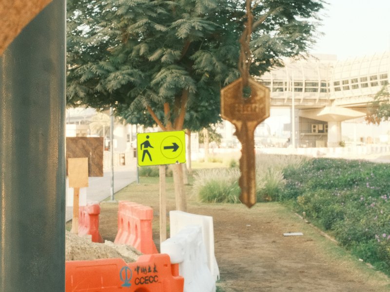 A pathway with construction barriers, a pedestrian sign pointing left, and trees in the background.