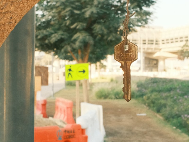 A close-up of a vintage key hanging in focus with a blurred urban background featuring construction signs.
