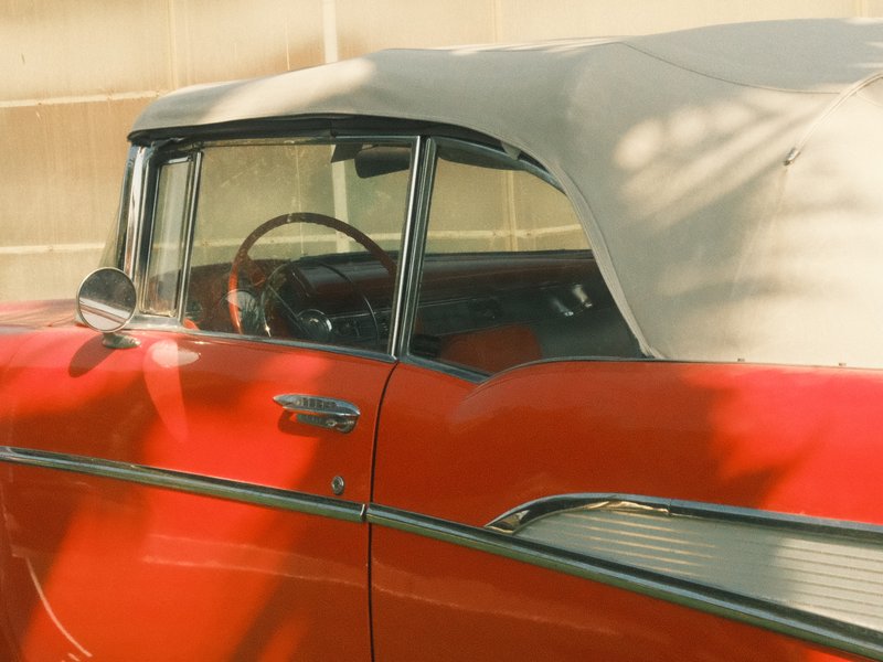 Close-up of a vintage red convertible car with a soft top, showcasing its interior and dashboard.