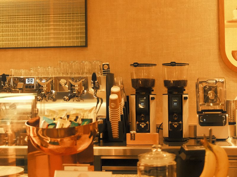 A cozy coffee shop counter with espresso machines, grinders, and decorative elements.