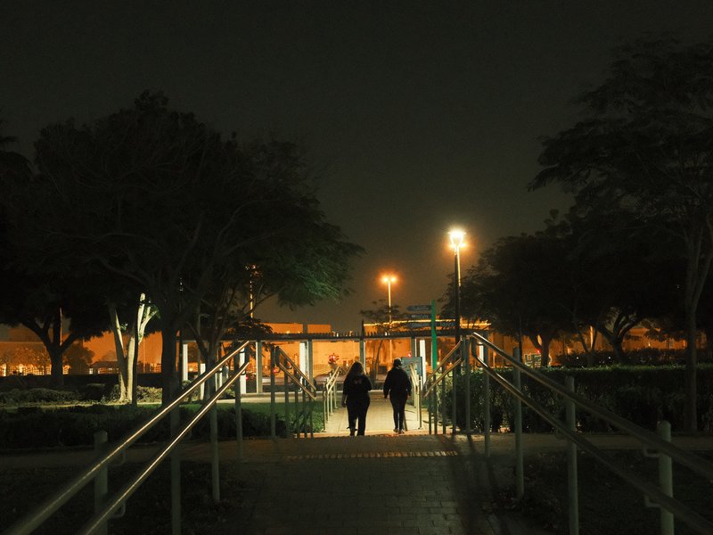Two silhouetted figures walking along a path in a park at night, illuminated by streetlights.