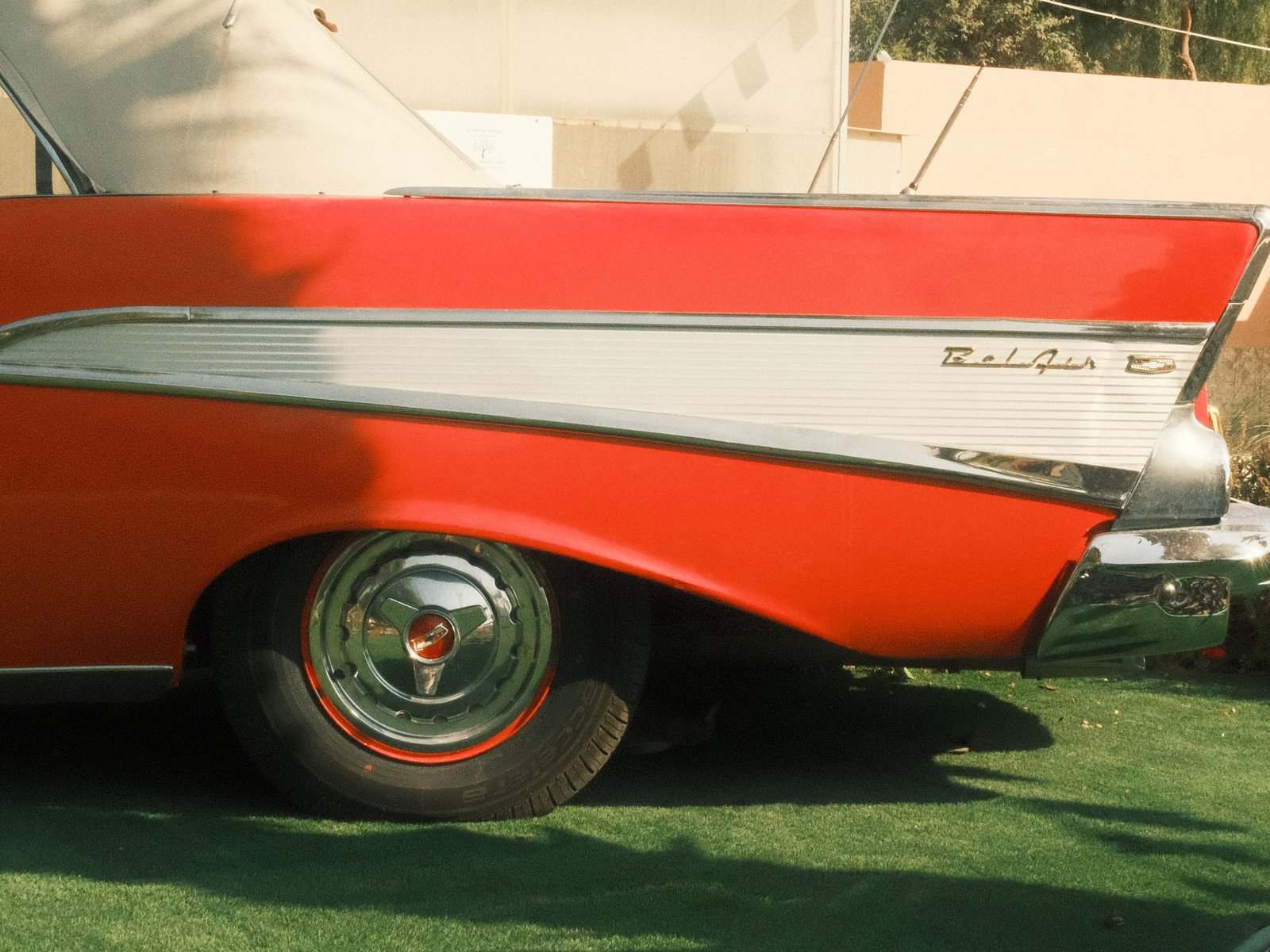Close-up of a classic red car's tail fin and wheel on green grass.