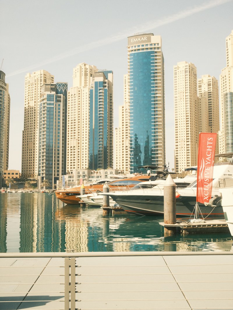 A view of modern skyscrapers reflecting in a marina with boats docked.