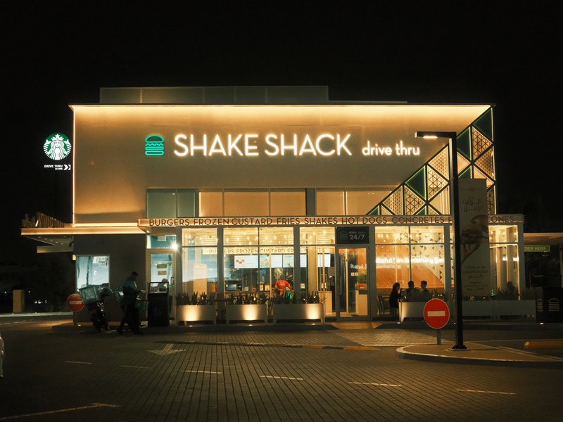 Exterior view of Shake Shack restaurant at night, illuminated signage and modern architecture.