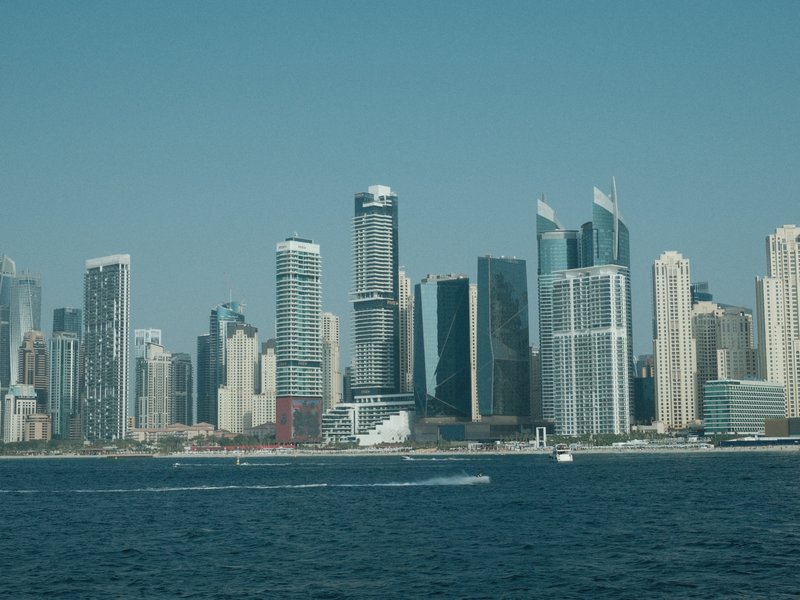 A skyline of tall buildings along a waterfront under a clear blue sky.