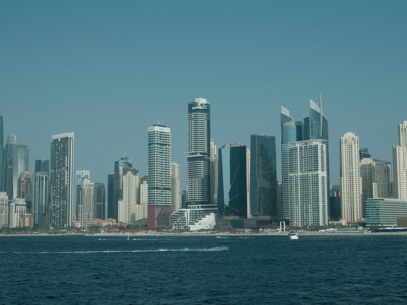 City skyline with modern skyscrapers against a clear blue sky, viewed from the water.