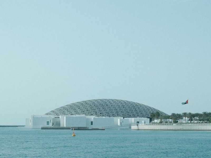 A modern architectural structure by the water with a dome and a clear sky.