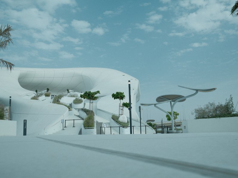 Modern architectural structure with white curves and trees under a cloudy sky.