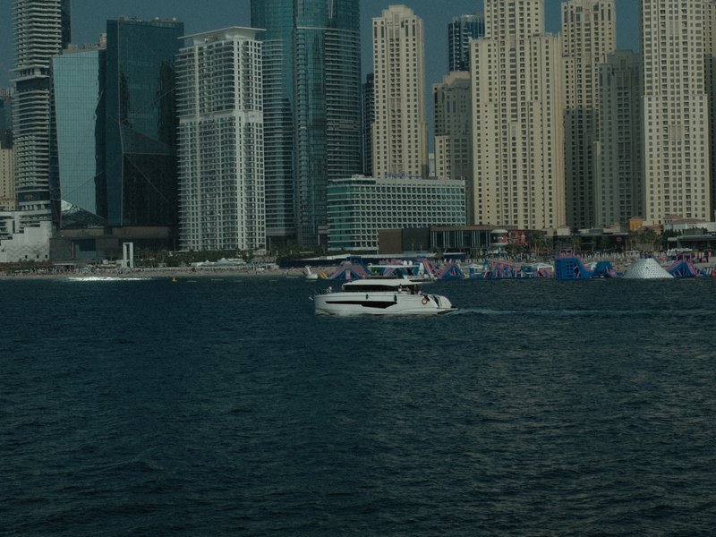 A boat cruising in a marina surrounded by tall skyscrapers and a clear blue sky.
