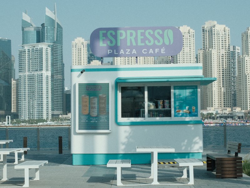 A colorful espresso kiosk by the waterfront with skyscrapers in the background.