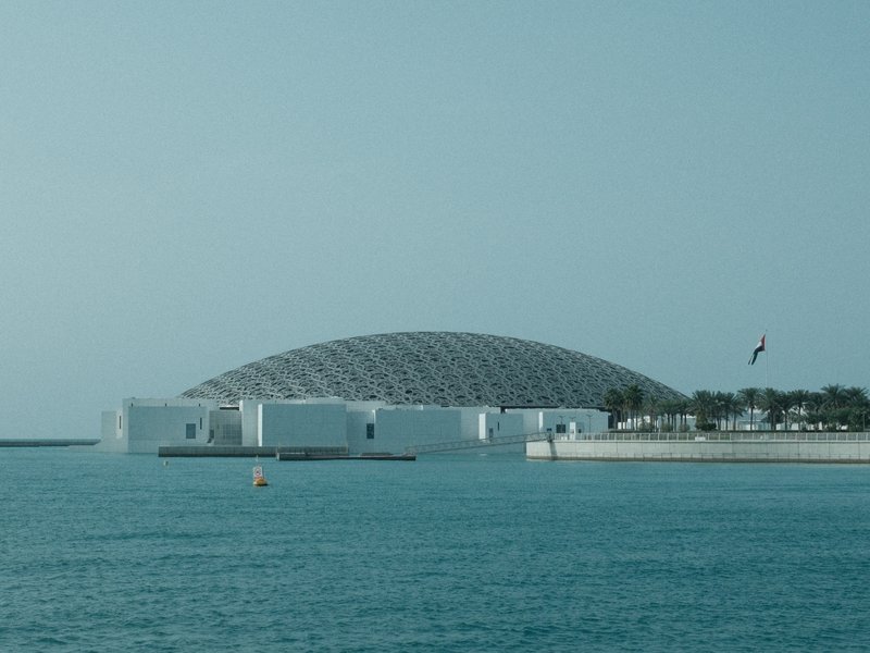 A modern architectural structure with a dome, situated by the water under a clear sky.