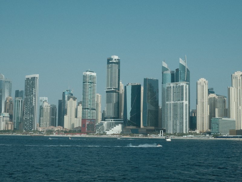 A skyline of tall buildings along a waterfront under a clear blue sky.