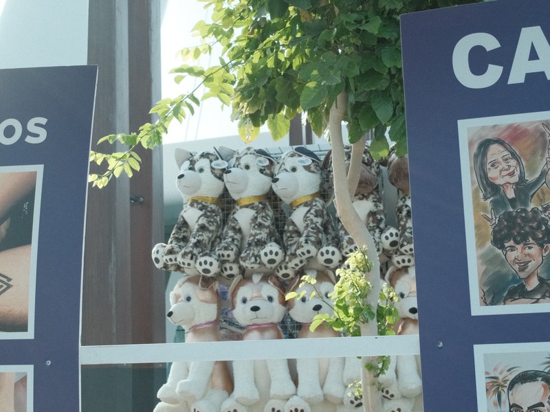A collection of decorative dolls displayed outdoors, surrounded by greenery and signage.