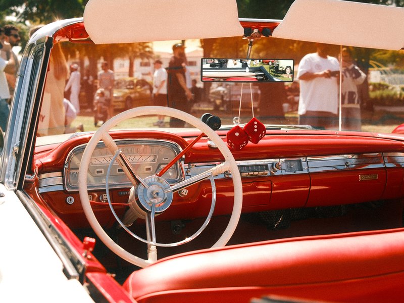 Interior view of a vintage car showcasing a red dashboard and steering wheel under warm sunlight.