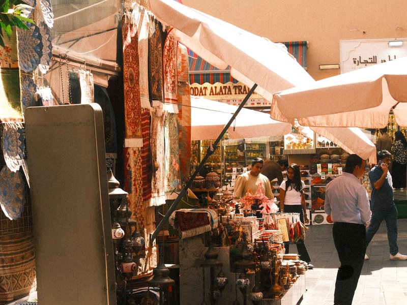 A bustling market scene with colorful textiles and goods under large umbrellas.