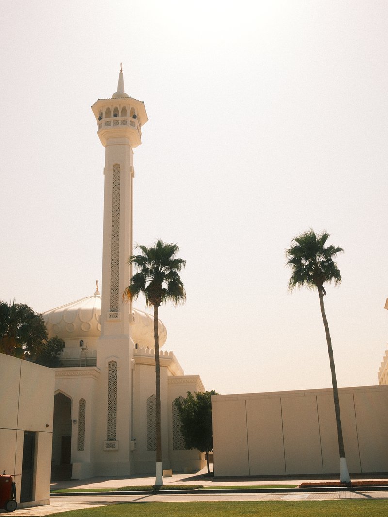 A tall minaret beside palm trees against a bright sky, showcasing architectural details.