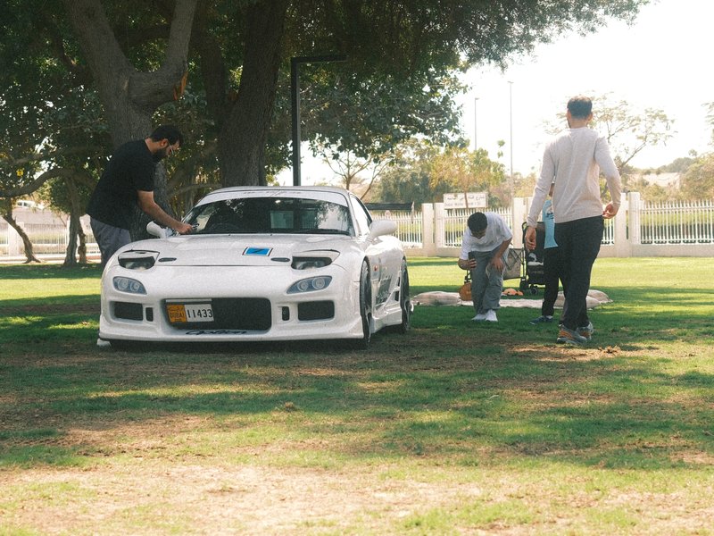 A white sports car parked on grass with three people working around it in a park.