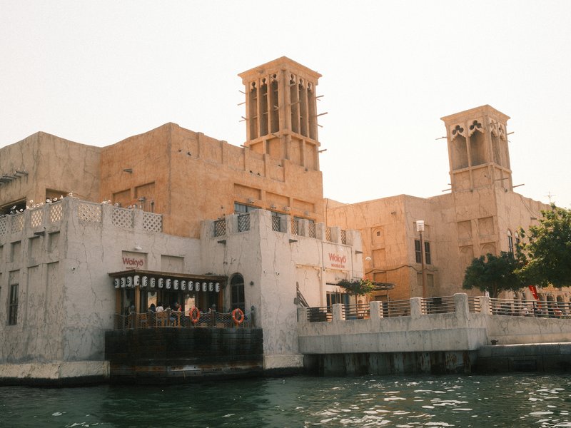 Historic building with wind towers beside a body of water, bathed in warm sunlight.