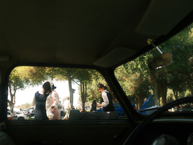 View from inside a car showing people interacting outside under trees.