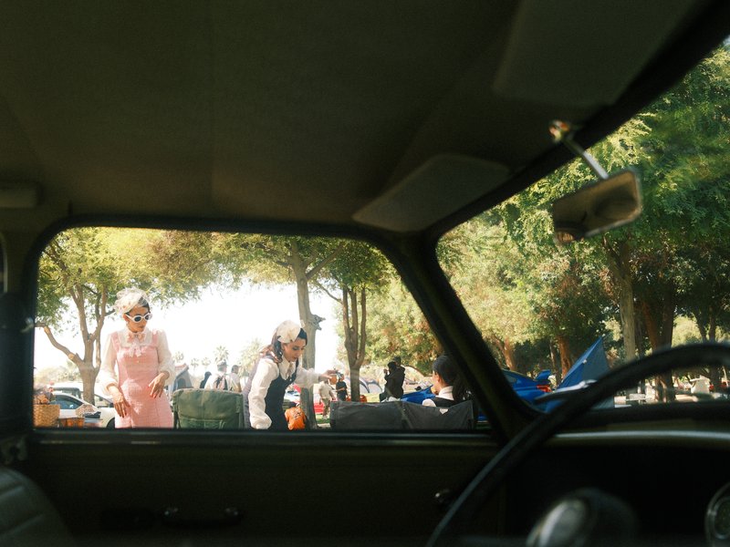 View from inside a car looking out at people in a park on a sunny day.