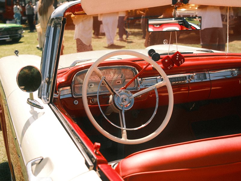 Interior view of a vintage car with a red and white color scheme, showcasing the steering wheel and dashboard.