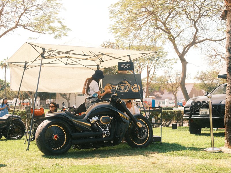 A custom motorcycle parked near a tent at an outdoor event with people in the background.