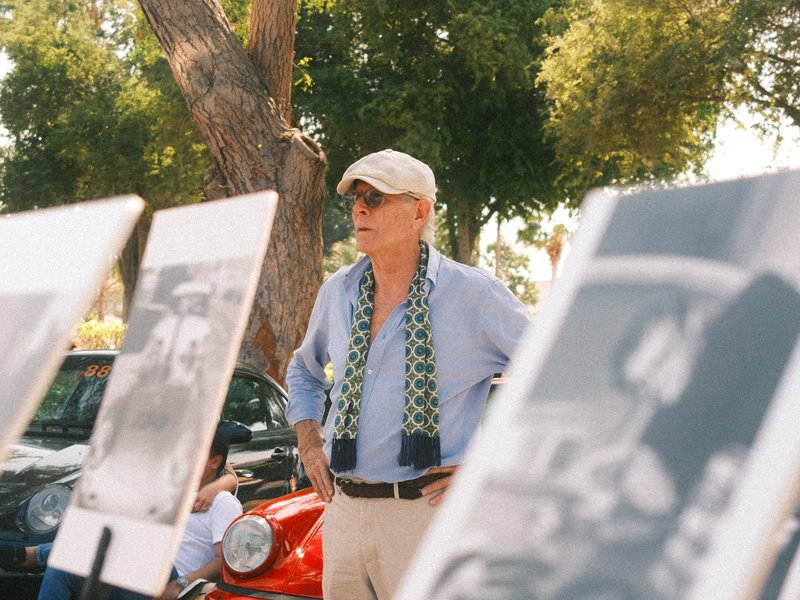 A man in a cap and sunglasses stands near photo displays in a sunny outdoor setting.
