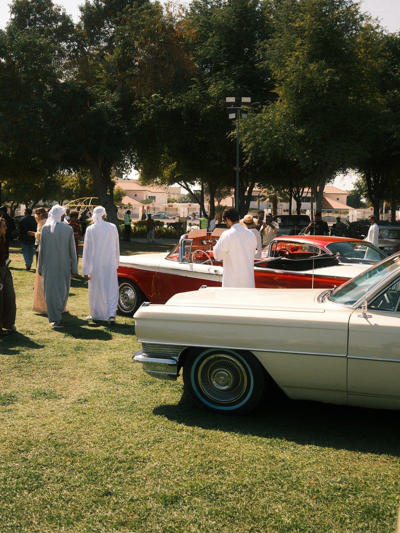 Classic cars on display at an outdoor event with people in traditional attire gathered around.