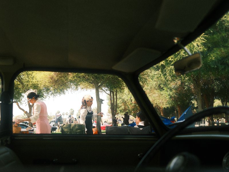 View from inside a car looking out at people in a park with trees and sunlight.