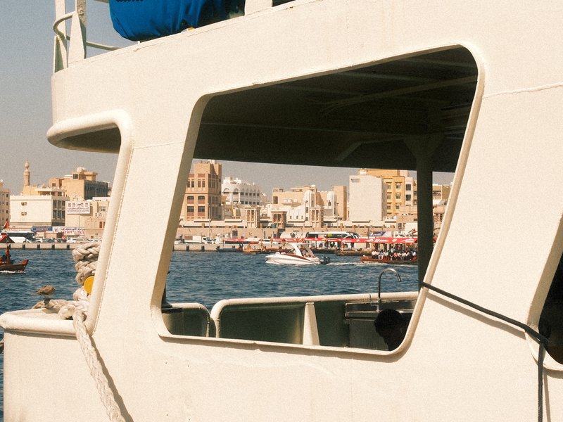 View through a boat's window showcasing a bustling harbor with boats and buildings in the background.