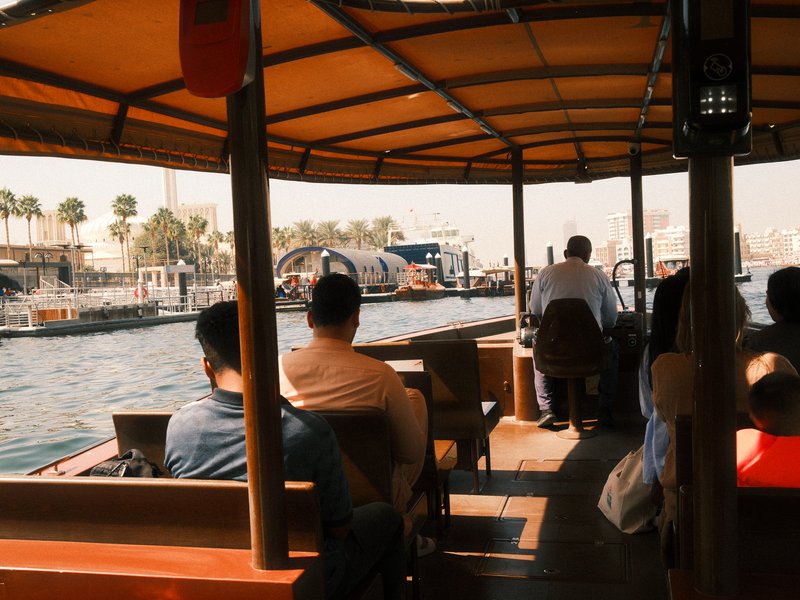 Passengers seated inside a boat, with a view of the waterfront and cityscape in the background.