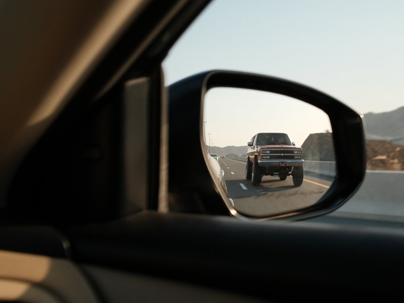 A view of a truck in the side mirror of a car on a highway during golden hour.